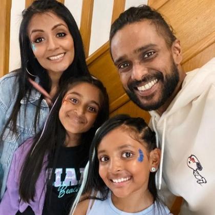 A family of four made up of a mother, father and two young girls. They are smiling together in their house