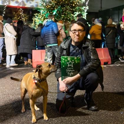 A man dressed in black crouching down, holding a CAL booklet. A dog is next to him.