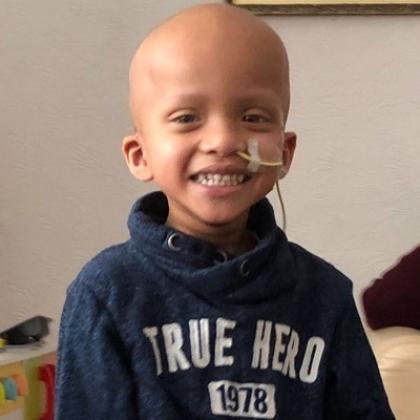 Head and shoulders of a young boy in a blue hoodie, smiling.