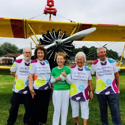 A group of five people wearing Royal Marsden Cancer Charity t-shirts and standing in front of a yellow propeller plane