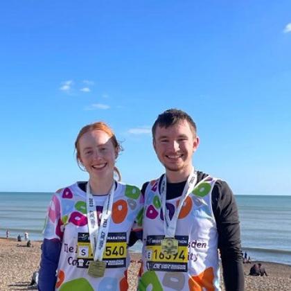 Two runners with medals in RMCC vests in front of the sea