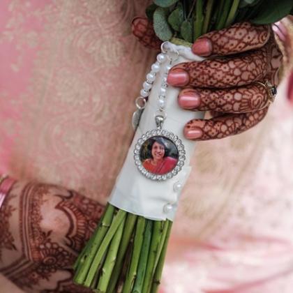 A bride's hands decorated in henna, holding flowers with a pendant of a woman's face