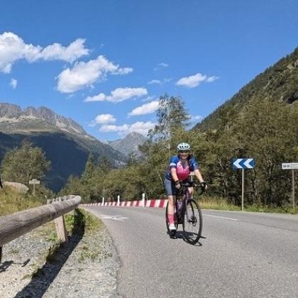 Jenni cycling on a road with beautiful scenery in the background - mountains on a bright blue, sunny day.