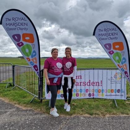 Two Team Marsden skydivers smile at an airfield, with Royal Marsden Cancer Charity flags behind them 
