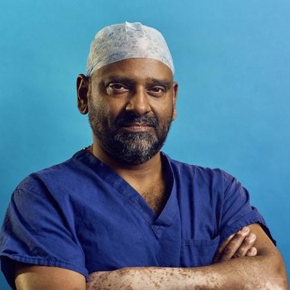 Headshot of Mr Shahnawaz Rasheed. He's wearing bright blue scrubs, a head cover and is folding his arms.