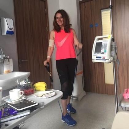 Shiona wearing gym clothing and standing in a hospital room at The Royal Marsden. She's using a tube resistance band 
