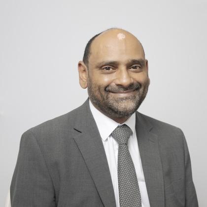 Headshot of Mr Shahnawaz Rasheed. He is smiling and wearing a formal grey suit jacket, pattered grey tie and white shirt.