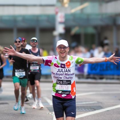 A Team Marsden runner during London Marathon 2025. He has his arms stretched out wide and is smiling
