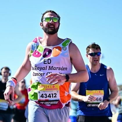 Royal Marsden runner, Ed, working hard on the sunny Brighton Marathon run with sunglasses on. There are blurred runners in the background.