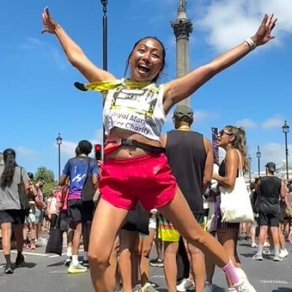 RMCC runner jumping in the air and smiling at the camera with a medal round her neck after finishing the run
