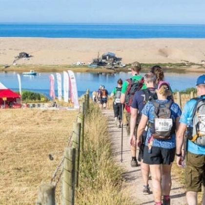 RMCC trekkers walking with poles and hats on with the sea in front of them