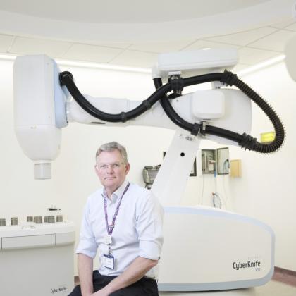 Professor Nicholas van As sitting next to the CyberKnife robot in Chelsea Hospital