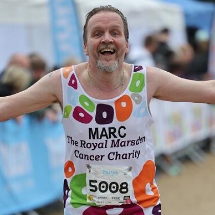Royal Marsden runner close up smiling with his arms out to his side as he crosses the finish line