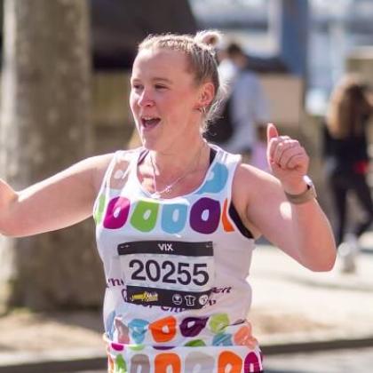 Royal Marsden runner smiling and doing a thumbs up to the crowd of supporters in the sun.
