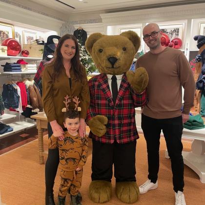 Tash, her husband and her son posing with a human-sized teddy bear in a department store