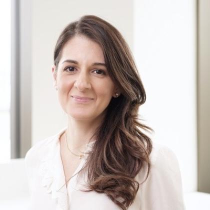 A headshot of Professor Christina Messiou. She has long, dark curled hair and is wearing a white blouse with a golden necklance