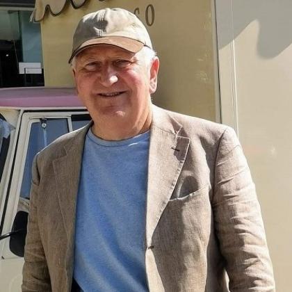 Philip smiling on holiday. He's wearing a beige jacket, cap and a light blue t-shirt