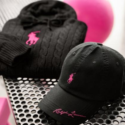 A selection of black clothing, including a jumper and a cap. They both have a pink version of the Ralph Lauren logo on them.