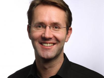 Portrait photo of Andrew Fisher. He is wearing a black shirt and glasses and is smiling. 
