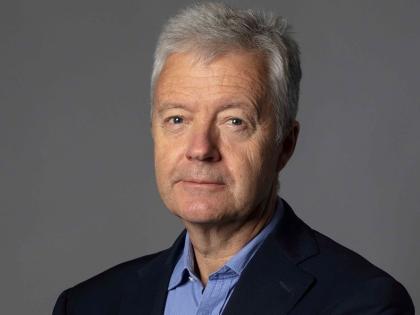 Headshot of Trustee, Russel Chambers. He has short grey hair and is wearing a blue shirt and black jacket.
