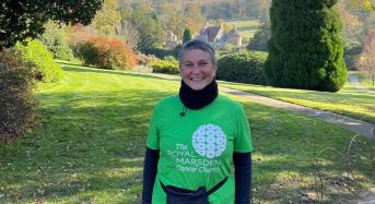 Middle age woman wearing a Green Royal Marsden shirt and smiling. She is outside