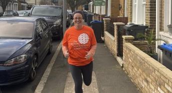 Jog 40 in January runner Claire. She is smiling and jogging through a residential street, wearing a bright orange Royal Marsden Cancer Charity t-shirt