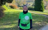 Middle age woman wearing a Green Royal Marsden shirt and smiling. She is outside
