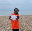 Jog 40 runner in her organge shirt on the beach. She is proudly showing off her completed mile tracker.