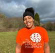 A smiling woman in an orange charity t-shirt and running leggings standing outside. 