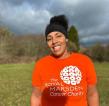 A smiling woman in an orange charity t-shirt and running leggings standing outside.