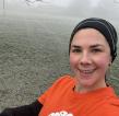 A selfie of a woman in a black headband and orange Royal Marsden Cancer Charity. She is running in a grassy field with frost covering it.