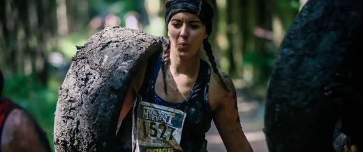 Mudnificent 7 woman participant carrying a large muddy tyre