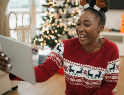 Image of a smiley, young black woman wearing a Christmas jumper and holding a virtual call by using her tablet.
