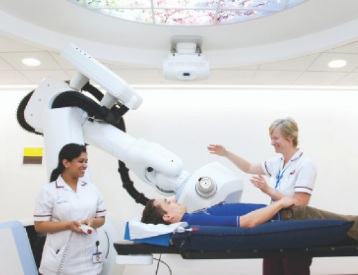 Image of a patient being assessed by two medical staff. The patient is shown the cyberknife.