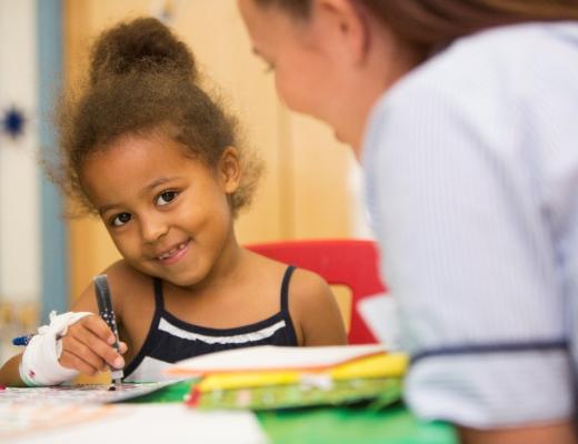 Young black child smiling and colouring with nurse