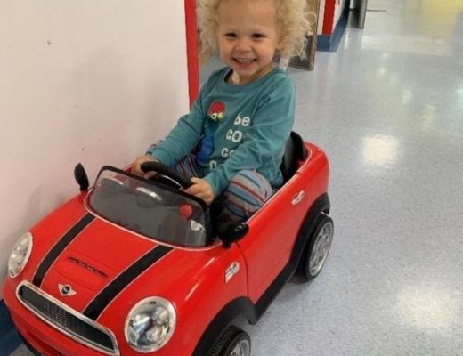 Child in a toy car in a hospital corridor