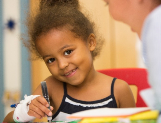 Child colouring whilst in hospital next to a nurse