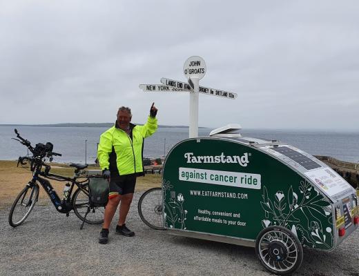 Simon Aylett poses at John O'Groats sign with his e-bike and mini caravan