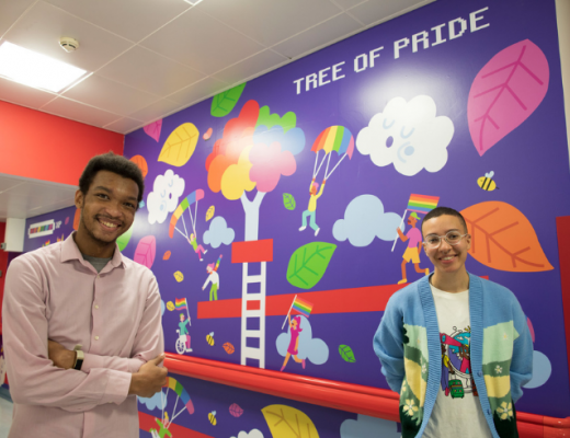 artist Ashton Attzs standing with Royal Marsden Youth Forum Member Joshua in front of the commissioned Tree of Pride inclusive mural