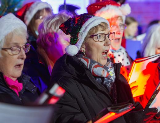 colourful photo of carol singers wearing Santa hats at a Celebrate A Life service