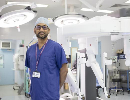 Professor Paleri in a surgical theatre. He is wearing blue scrubs, glasses. 