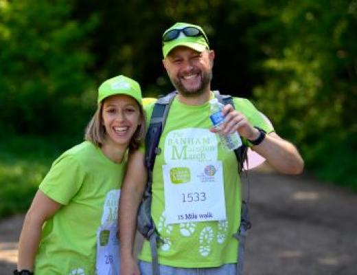 A smiling couple wearing Banham Marsden March t-shirts and caps on a woodland trail