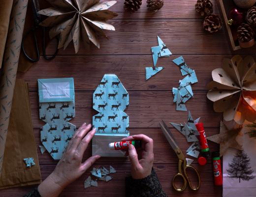 A top down angle photo of pair of hands making a Christmas craft paper snowflake. 