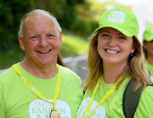 A man and woman smiling. They are wearing Green Banham Marsden March shirts and caps. 