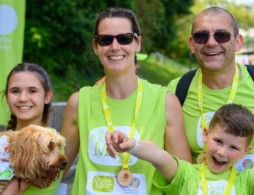 A smiling family with parents, two young children and their dog at the finish live of The Banham Marsden March. 