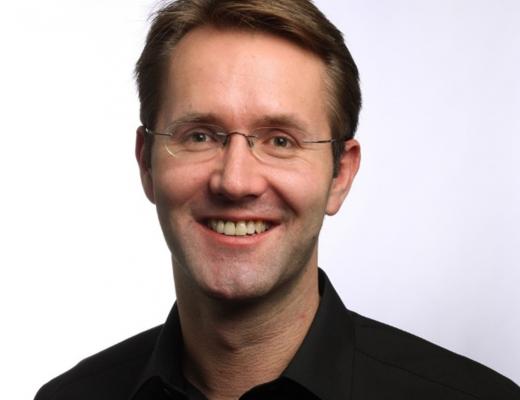 Portrait photo of Andrew Fisher. He is wearing a black shirt and glasses and is smiling. 