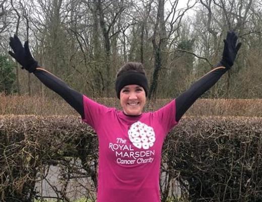 A woman standing outside in running gear. She is smiling and has her hands in the air and is wearing a bright pink Royal Marsden Cancer Charity t-shirt. 