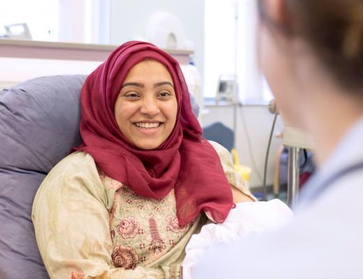 A patient at The Royal Marsden in a treatment chair. She is wearing a red headscarf and smiling. 