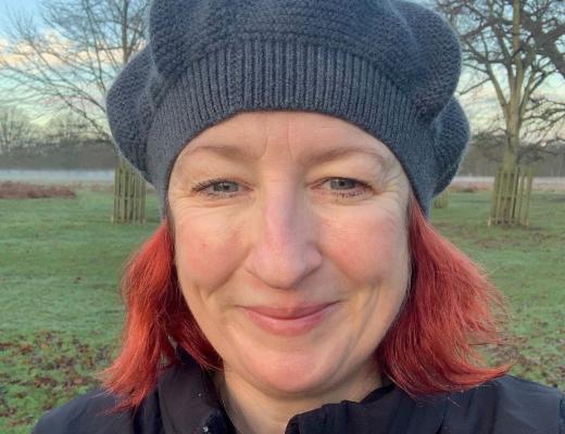 A photo of Pip smiling. She has A grey knitted hat on and bright red hair. 