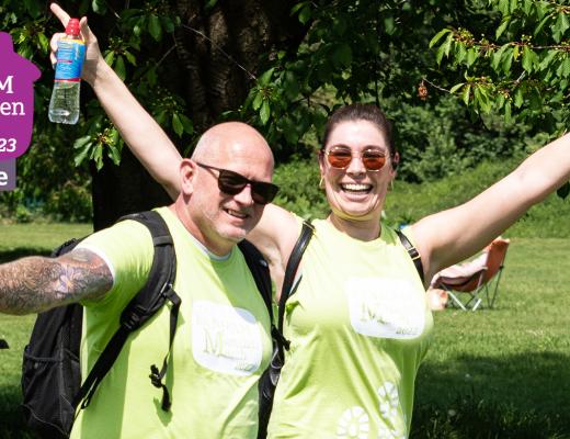 A Man and woman smiling. They are outside in the sunshine wearing green Banham Marsden March t-shirts